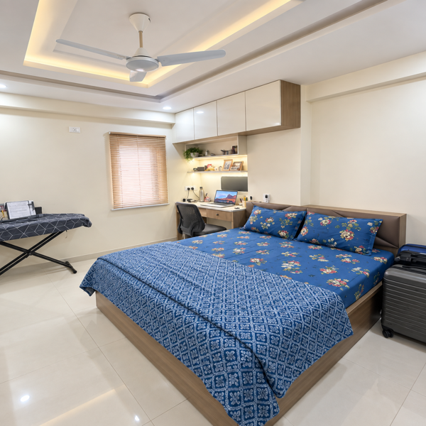 Modern bedroom, stylish bedroom, cozy bedroom, elegant interior, contemporary home, bedroom decor, interior design, blue bedspread, floral bedding, king size bed, comfortable bed, decorative pillows, blue cushions, wooden bed frame, study desk, work from home, laptop desk, office chair, wall shelves, storage cabinets, wooden furniture, bedroom furniture, ceiling fan, false ceiling, recessed lighting, warm lighting, window blinds, spacious bedroom, clean room, organized interior, minimalist decor, modern apartment, luxury bedroom, residential interior, home decor, bright room, glossy flooring, tiled floor, suitcase, travel luggage, bedside space, wall storage, compact workspace, stylish home, peaceful bedroom, comfortable living, contemporary decor, neat interior, functional bedroom, modern lifestyle, sophisticated room, indoor photography.